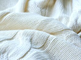 Cable Knit Pure Cashmere Fabric Close-up of a folded off-white cashmere blanket with a prominent cable knit pattern, showing textured stitches and depth from light and shadow.