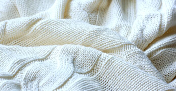 Cable Knit Pure Cashmere Fabric Close-up of a folded off-white cashmere blanket with a prominent cable knit pattern, showing textured stitches and depth from light and shadow.