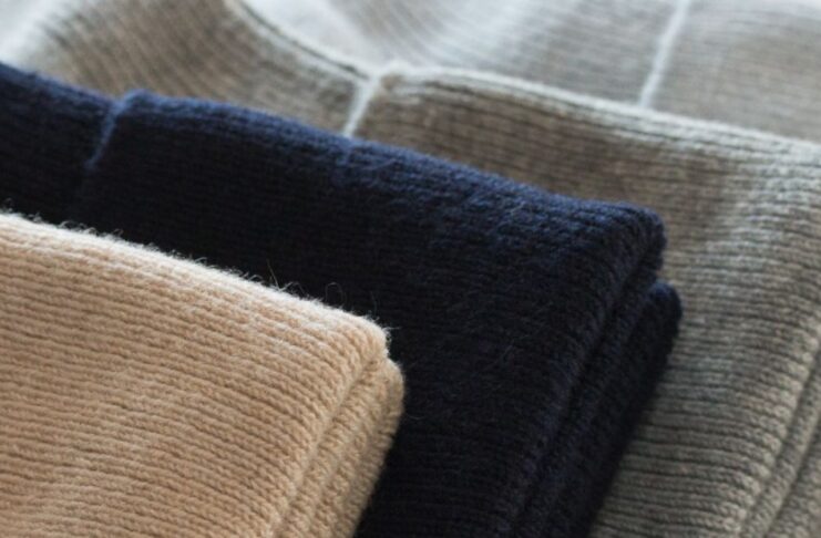 Cashmere-Cotton Blend Close-up of folded cashmere-cotton blend sweaters in beige, black, and gray.