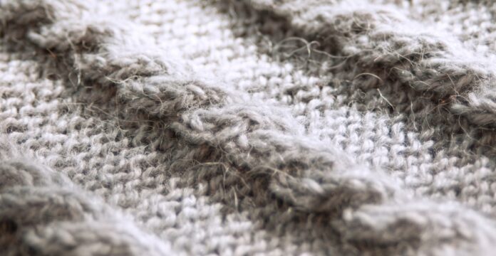 Cashmere Twill Fabric Guide Close-up of a grey knitted wool fabric with a textured cable knit pattern; soft, slightly fuzzy fibers with a subtle sheen.