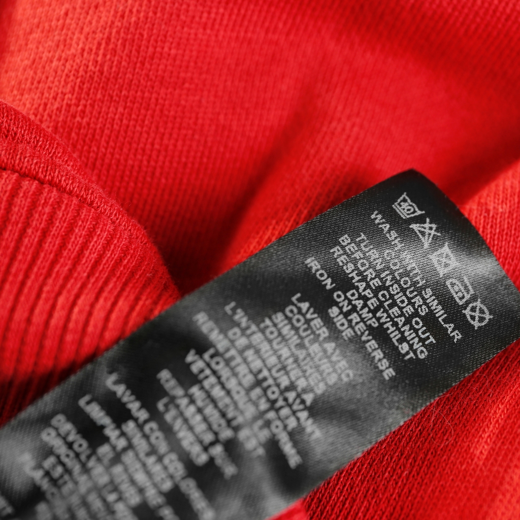 Insulated Softshell Jacket: Lightweight Warm Outdoor Wear 4 Close-up of a black care label on a red knitted fabric, showing washing instructions.