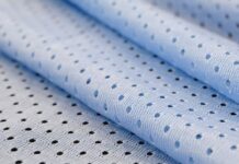 Cool Max Air Flow Mesh Fabric: High-Performance Ventilation Close-up of light blue athletic mesh fabric with a repeating pattern of small circular holes. The fabric is folded, showing its texture and weave.Cool Max Air Flow Mesh Fabric: