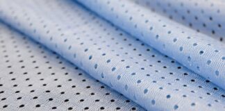 Cool Max Air Flow Mesh Fabric: High-Performance Ventilation Close-up of light blue athletic mesh fabric with a repeating pattern of small circular holes. The fabric is folded, showing its texture and weave.Cool Max Air Flow Mesh Fabric:
