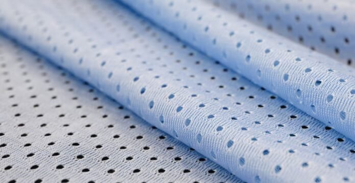 Close-up of light blue athletic mesh fabric with a repeating pattern of small circular holes. The fabric is folded, showing its texture and weave.Cool Max Air Flow Mesh Fabric: