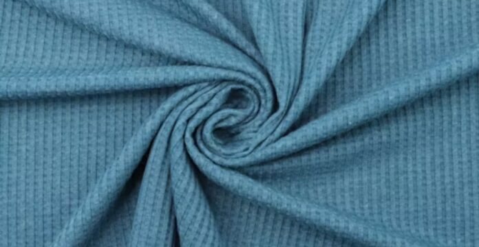 Close-up of light blue waffle knit fabric arranged in a swirling fold, showing a grid-like texture with shadows and highlights. Power Stretch Active Fabric: