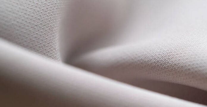 Close-up of folded light grey fabric with a subtle texture and soft lighting. Flex Motion Stretch Fabric: