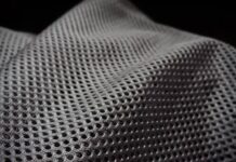 Air Mesh Pro Performance Fabric: Breathable Sportswear Guide Close-up of a gray, net-like fabric with a grid of small, evenly spaced holes and subtle folds. The background is dark and blMaximum Warmth Winter Coat fabric texture: close-up of a gray mesh-like material. urry.Air Mesh Pro Performance Fabric: