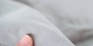Chill Tech Moisture Control Fabric: Cooling Comfort All Day Alt text: A close-up of light gray fabric with a subtle repeating pattern, slightly bunched, with a finger touching the fabric in the lower left corner. Chill Tech Moisture Control Fabric: