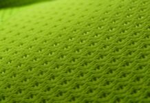 MotionX Breathable Sports Fabric: Performance Meets Comfort "Close-up of bright green synthetic mesh fabric with a repeating pattern of small interconnected holes for breathability, and a left edge strip with larger circular perforations." MotionX Breathable Sports Fabric: