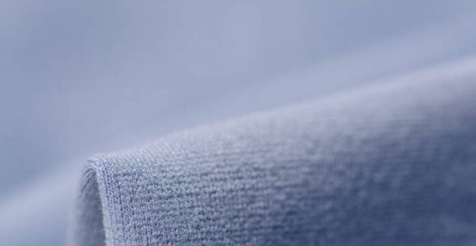 Alt text: “A close-up view of a soft, blue knit fabric that resembles the texture of a winter coat or warm fleece, with a rolled edge in the foreground.” Frost Flex Active Fabric: