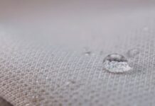 Chill Pro Moisture-Wicking Fabric Explained: Benefits & Uses "Close-up of light gray fabric with water droplets. A large droplet in focus shows a distorted reflection of the woven texture, with several smaller droplets nearby." Chill Pro Moisture-Wicking Fabric Explained: