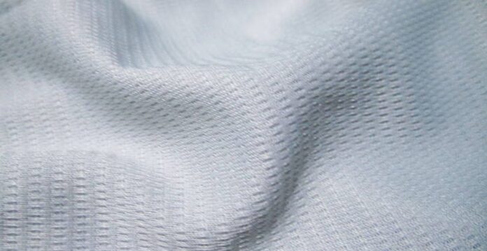 Close-up of soft, light-gray knit fabric with tight stitching, labeled “Maximum Warmth Winter Coat.”Ice Flow Athletic Fabric: