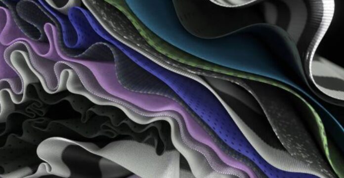 Close-up view of multiple layered fabrics in wavy, overlapping folds. Colors include purple, blue, green, and silver, with a mix of mesh-like and smooth textures. Soft, diffused lighting highlights the depth and texture of the folds. ProFit Compression Tech Fabric