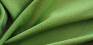 Ventra Cool Training Fabric: Stay Cool, Dry, Perform Better A close-up photograph of a bright green, textured fabric with small perforations. The fabric is folded in soft, overlapping layers, creating smooth curves and subtle shadows that emphasize its breathable, mesh-like weave.