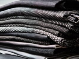 Quantum Flex Performance Fabric: Move Better, Perform Better A stack of folded dark-colored technical fabrics with textured weaves, showcasing layered materials commonly used in performance or outerwear garments.Quantum Flex Performance Fabric: