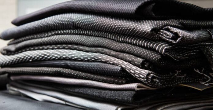 A stack of folded dark-colored technical fabrics with textured weaves, showcasing layered materials commonly used in performance or outerwear garments.Quantum Flex Performance Fabric: