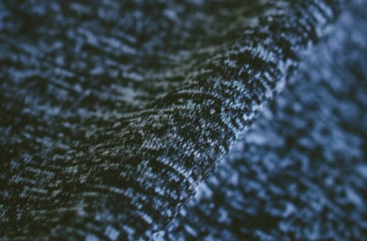 "Close-up of textured winter coat fabric showing a subtle interplay of dark and light fibers in a soft, lofty knit structure with visible depth from gentle draping." Ice Flux Performance Knit:
