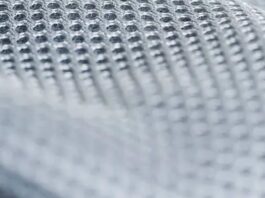 Close-up of a light gray/white technical mesh fabric with a uniform grid of small, evenly spaced perforations; texture is sharply defined at the top and softly blurred toward the bottom. Frost Flex Cooling Fabric:
