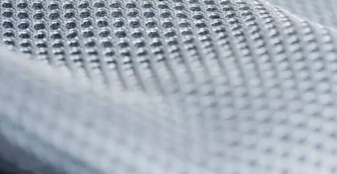 Close-up of a light gray/white technical mesh fabric with a uniform grid of small, evenly spaced perforations; texture is sharply defined at the top and softly blurred toward the bottom. Frost Flex Cooling Fabric: