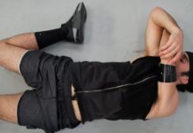 Kinetic Flow Athletic Fabric: Ultimate Comfort for Athletes "A man lies on his back on a gray floor wearing a black beanie, sleeveless shirt, shorts, black socks, shoes, and a black wristband; left hand near face." Kinetic Flow Athletic Fabric: