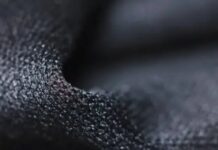 Quantum Dry Sports Fabric: Revolutionizing Athletic Comfort Close-up of dark, granular-textured fabric with pronounced 3D surface structure, showing highlights and shadows. Quantum Dry Sports Fabric