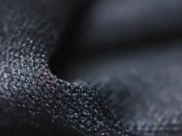 Close-up of dark, granular-textured fabric with pronounced 3D surface structure, showing highlights and shadows. Quantum Dry Sports Fabric
