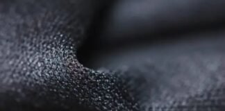Quantum Dry Sports Fabric: Revolutionizing Athletic Comfort Close-up of dark, granular-textured fabric with pronounced 3D surface structure, showing highlights and shadows. Quantum Dry Sports Fabric