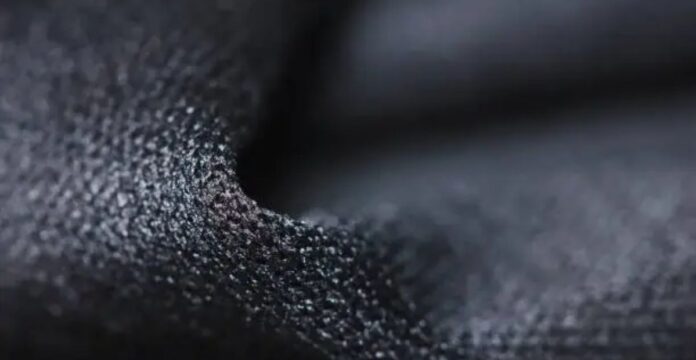 Close-up of dark, granular-textured fabric with pronounced 3D surface structure, showing highlights and shadows. Quantum Dry Sports Fabric