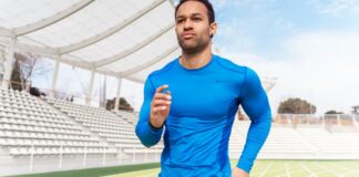 Power Fit Compression Fabric: Ultimate Support for Athletes A man in a bright blue athletic long-sleeve shirt runs on a track in a stadium with empty white seats and a clear sky in the background. Power Fit Compression Fabric:
