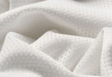 Flex Pro Sports Fabric: High-Performance Fabric for Athletes Close-up of white, textured fabric with tiny perforations arranged in a subtle repeating pattern, draped in soft folds to show light and shadow.Flex Pro Sports Fabric: