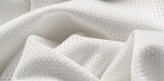 Flex Pro Sports Fabric: High-Performance Fabric for Athletes Close-up of white, textured fabric with tiny perforations arranged in a subtle repeating pattern, draped in soft folds to show light and shadow.Flex Pro Sports Fabric: