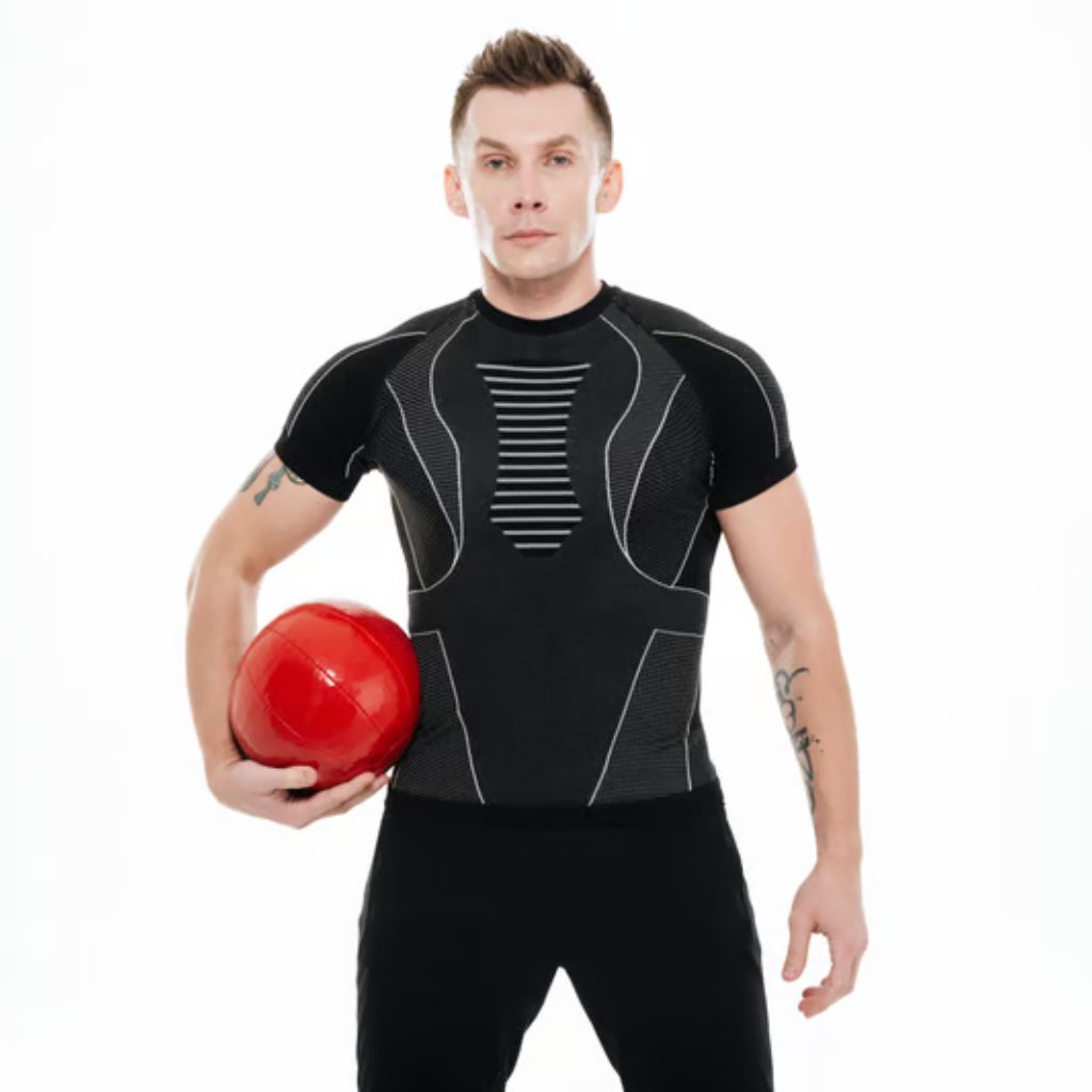 A man in athletic black gear stands against a white background, holding a shiny red ball in his right hand. He has short brown hair, a neutral expression, and visible tattoos on both arms.
Power Fit Compression Fabric: