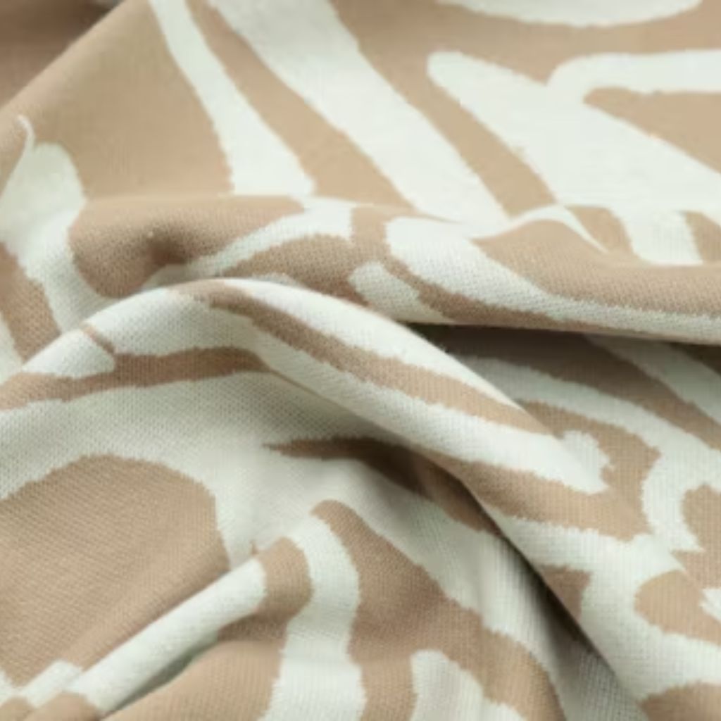 Close-up of a beige and white patterned blanket with abstract zebra-like stripes, showing soft wrinkles and textured knit.

Power Stretch Active Fabric: