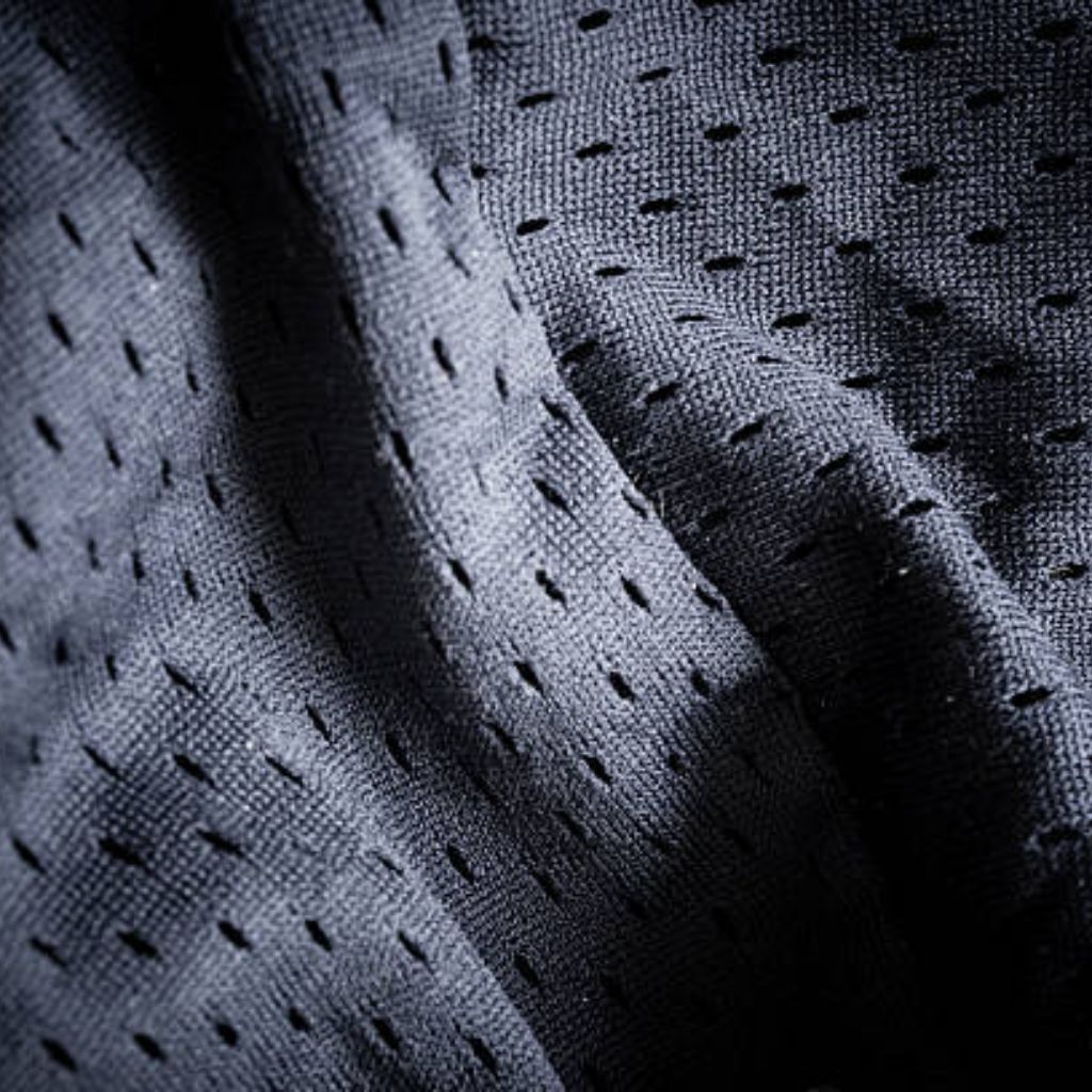 Close-up of a dark blue or black jersey mesh fabric with small, evenly spaced holes. The fabric is folded, creating shadows and highlights.
Air Mesh Pro Performance Fabric: