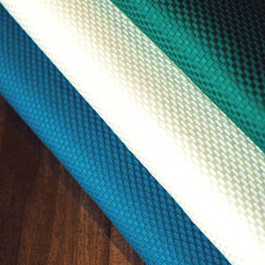 Quantum Flex Performance Fabric: Move Better, Perform Better 10 Close-up of textured mesh performance fabric rolls in teal, blue, and white on a wooden surface.Quantum Flex Performance Fabric: