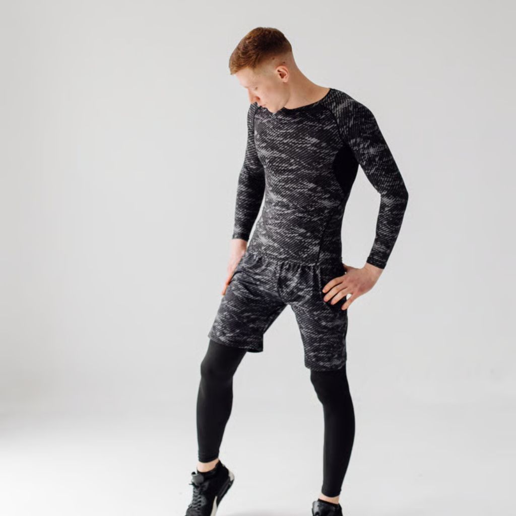 A man with red hair stands against a white background, wearing a gray mottled long-sleeve shirt, matching shorts, black leggings, and black athletic shoes. He looks down and to the side.
Gym and Fitness Training Outfits: