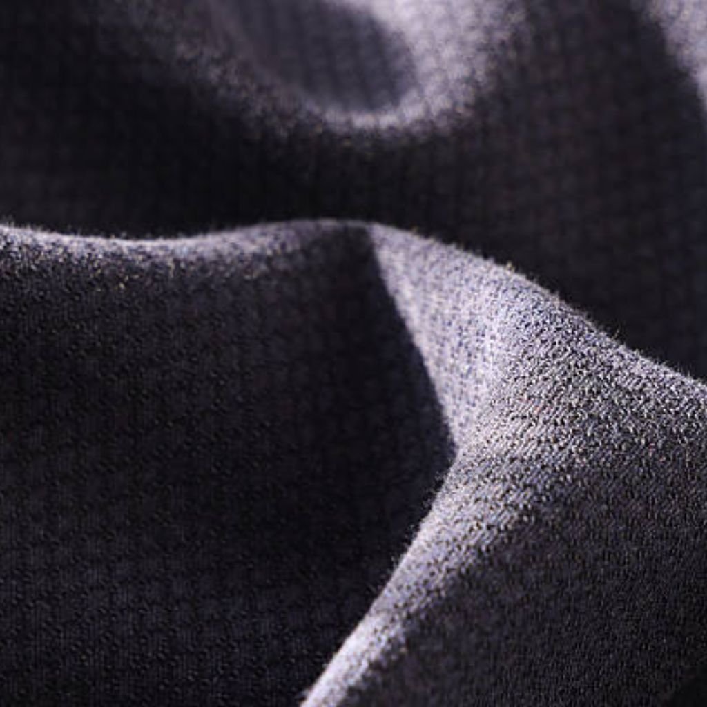 "Close-up of dark gray textured fabric with soft folds and draping, showing light and shadow across the surface and a slightly rough, bumpy texture."
Chill Pro Moisture-Wicking Fabric Explained:
