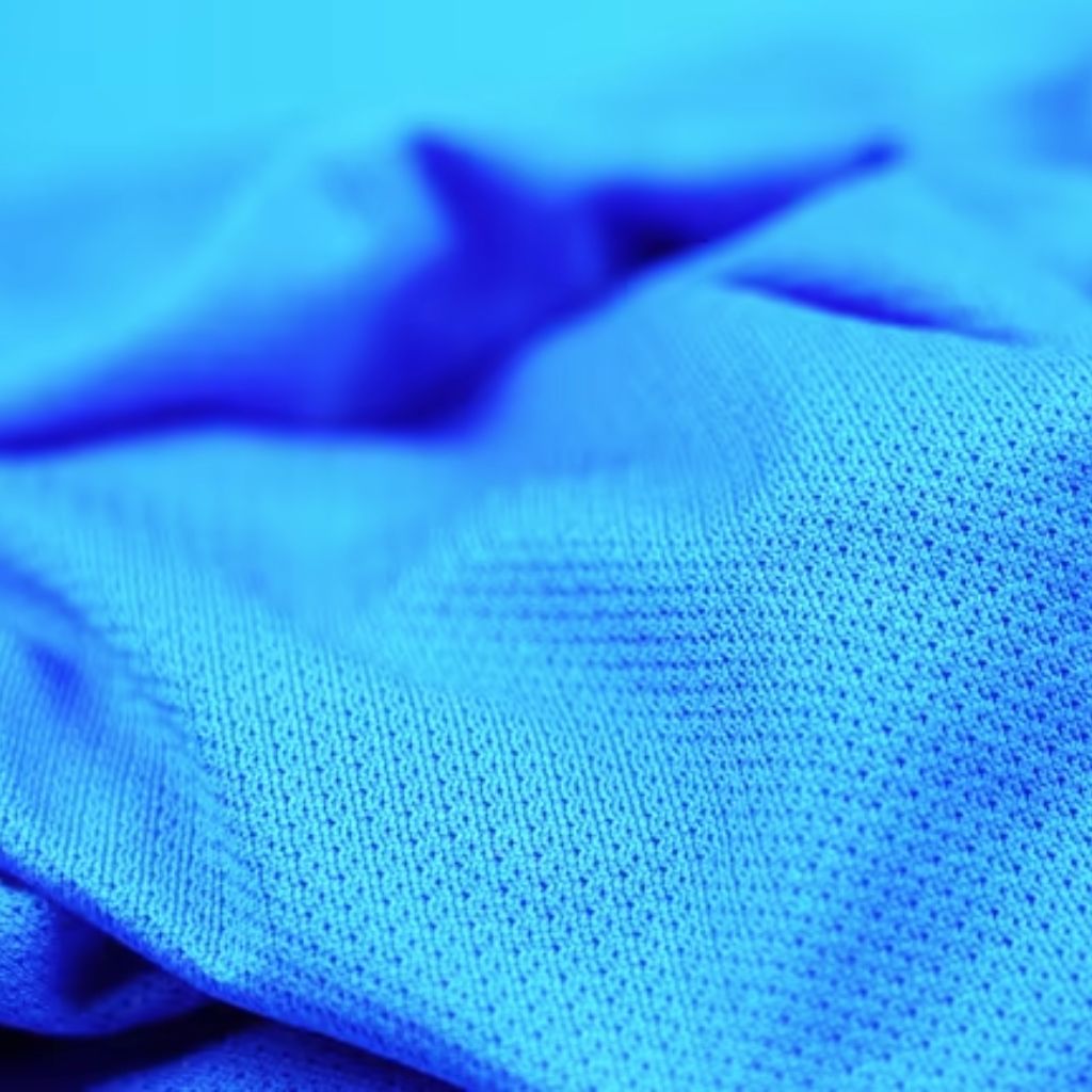 Close-up of bright blue fabric with a perforated, textured pattern, draped into soft folds.Hydro Wick Active Fabric:
