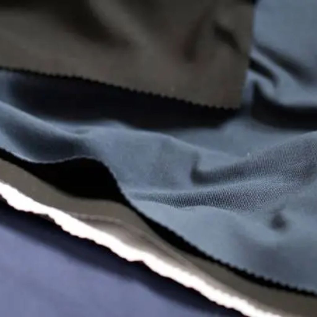 Close-up of layered fabric in blue, gray, and white tones. Visible folds and interwoven threads with a rough fringe along one edge.Hyper Stretch Athletic Fabric:
