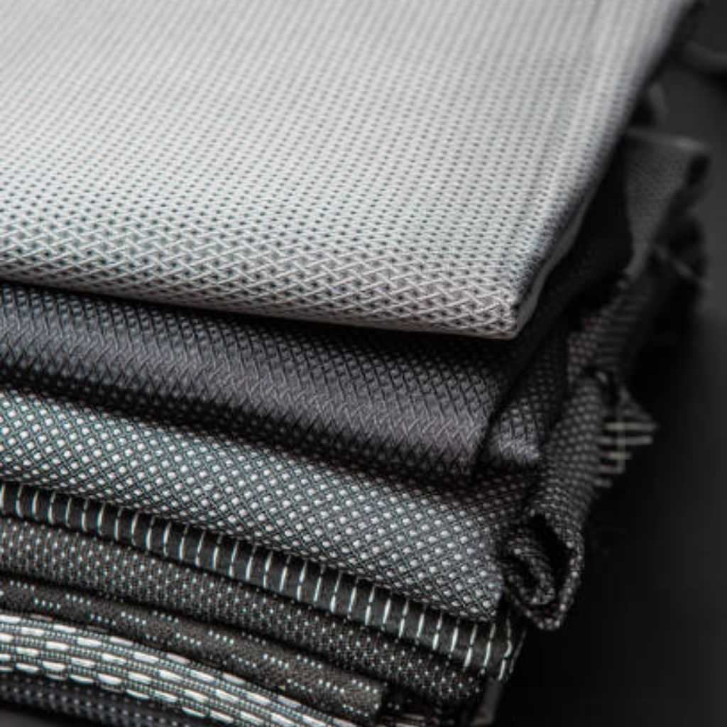 Quantum Flex Performance Fabric: Move Better, Perform Better 11 Stack of folded textured fabrics in shades of gray, featuring mesh-like and geometric weave patterns.Quantum Flex Performance Fabric: