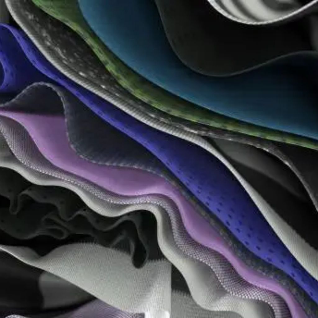 "Close-up of layered fabric swatches in blue, green, purple, grey, and black with wavy folds, varied textures, and subtle perforations."
Quantum Dry Sports Fabric
