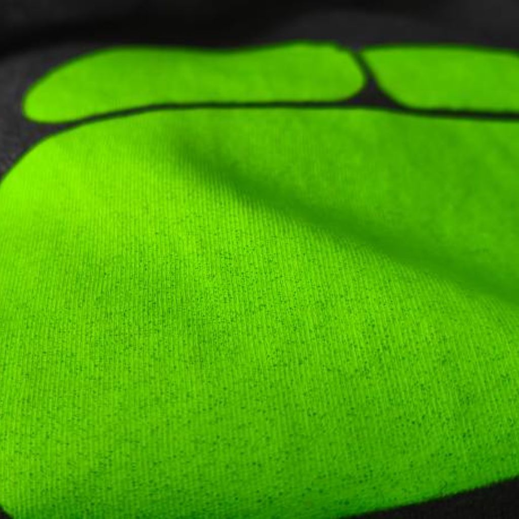 Close-up of a lime green footprint graphic printed on dark gray fabric. The print shows a large toe and two smaller toes separated by a black line, with a slightly grainy texture against a smooth backgrounProFit Compression Tech Fabricd.
