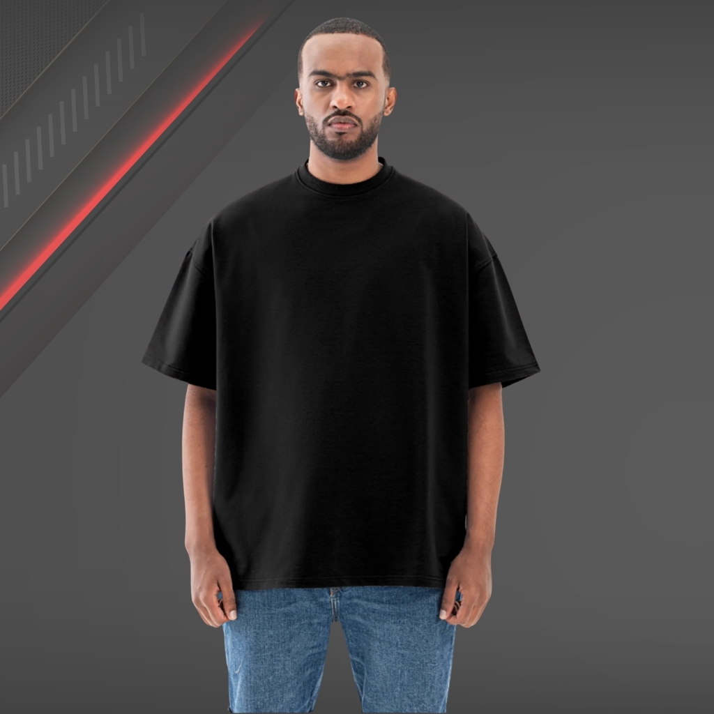 What Is a T-Shirt , Types and Style Guide 14 Man wearing an oversized black T-shirt with a relaxed fit and blue jeans, standing in front of a dark studio background with a red diagonal accent.