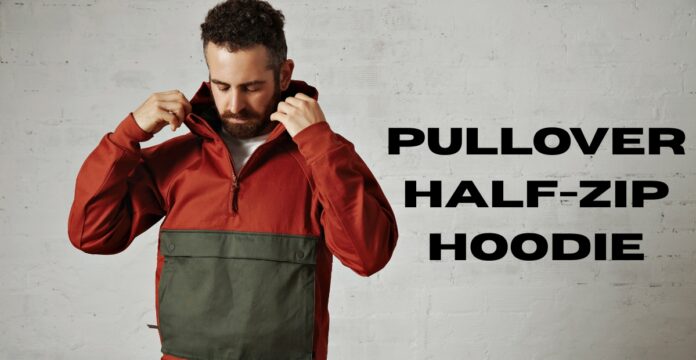A man wearing a two-toned pullover hoodie (rust-colored top half and olive green bottom half) adjusts the hood while standing against an off-white, slightly textured wall. Large black text to the right reads “PULLOVER HALF-ZIP HOODIE.”