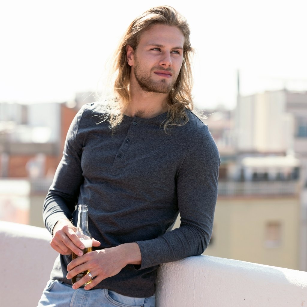 Henley T-Shirts for Men Stylish Button Neck Casual Wear 4 Man wearing a dark henley t-shirt outdoors on a rooftop holding a bottle.