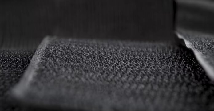 Black Velcro hook-side fastener: dense, interwoven nylon hooks with pronounced texture and strong dimensional depth under directional lighting. Velocity Dry Tech Knit: