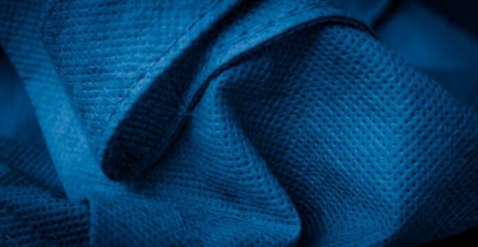 Close-up of deep blue micro-perforated fabric used in a winter coat, showing evenly spaced breathable holes and folded texture. Polar Air Breathable Fabric: