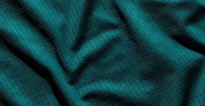 Close-up of a teal synthetic winter coat fabric with a subtle grid-pattern of perforations, shown draped with visible texture, shadows, and highlights. Turbo Dry Athletic Fabric: