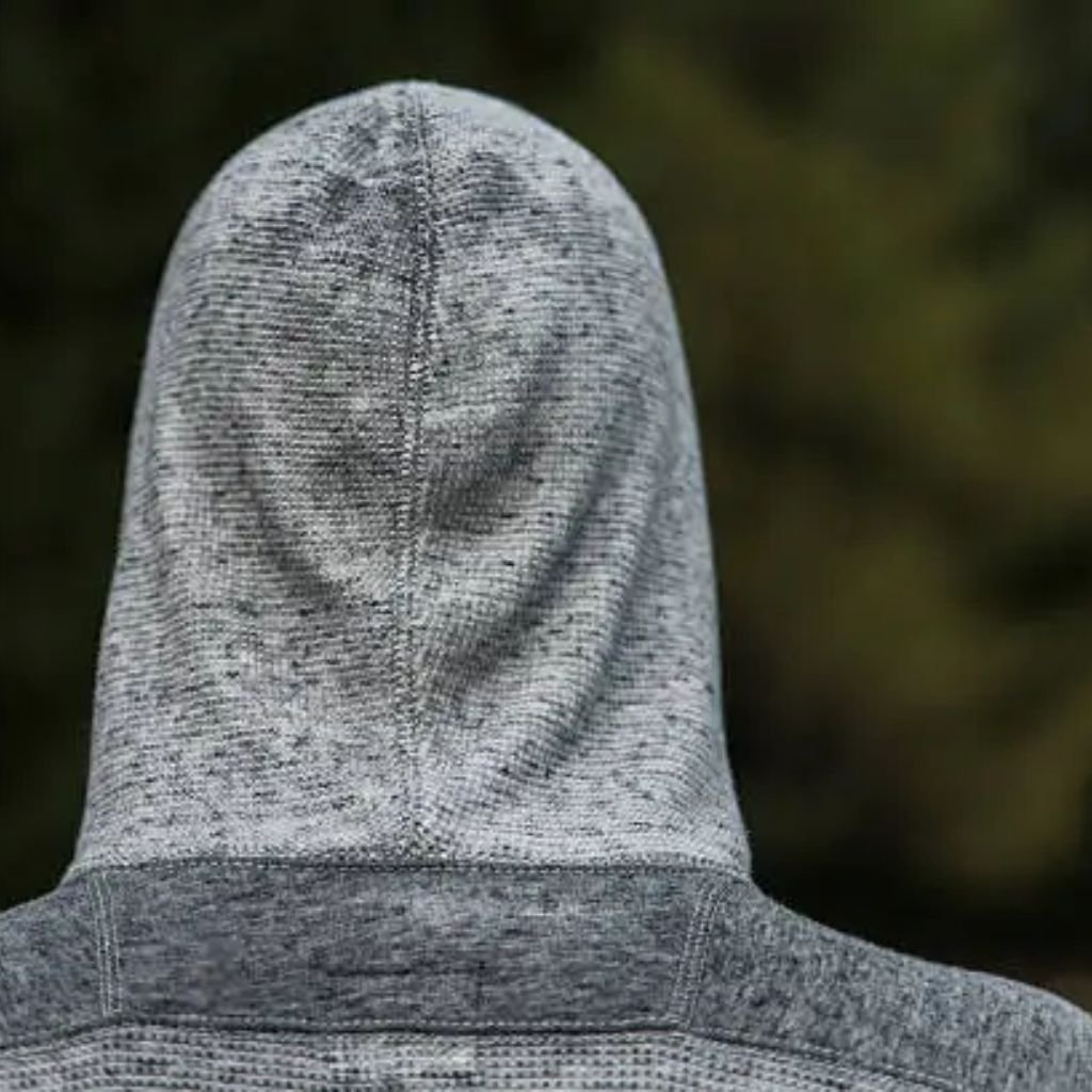 Sweat Shield Performance Knit:Concise, objective, and functional — focuses on what’s visually present and meaningful.

A person from behind wearing a gray heathered hooded sweatshirt with the hood up; soft, blurred green foliage in the background suggests an outdoor forest setting.