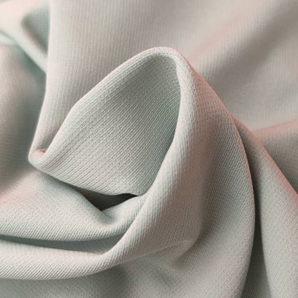 "Close-up of pale green textured fabric with subtle ribbing, artfully draped in soft folds that create gentle shadows, emphasizing its matte finish and tactile weave" Power Stretch Elite Fabric: